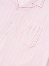 The Pink Lily Stripe Road Shirt is shown from the back, worn by a model. The shirt features a camp collar and short sleeves, with a vertical stripe pattern in shades of pink, white, and red. The model is also wearing olive green trousers. The background is a plain, neutral light gray.