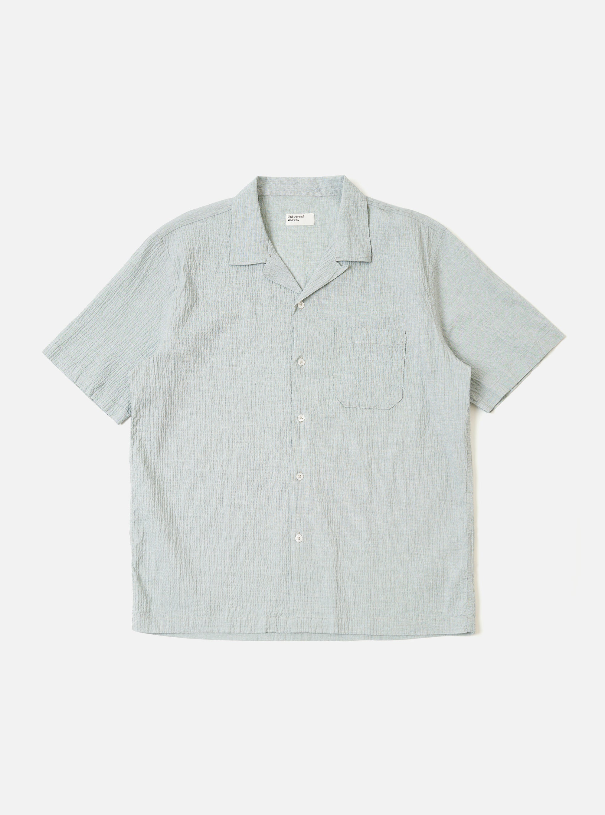 The Green Seersucker Road Shirt is shown as a flat lay against a white background. The shirt features a camp collar, a button-front closure with tonal buttons, and a straight hem. The fabric has a distinctive puckered seersucker texture in a solid green color.