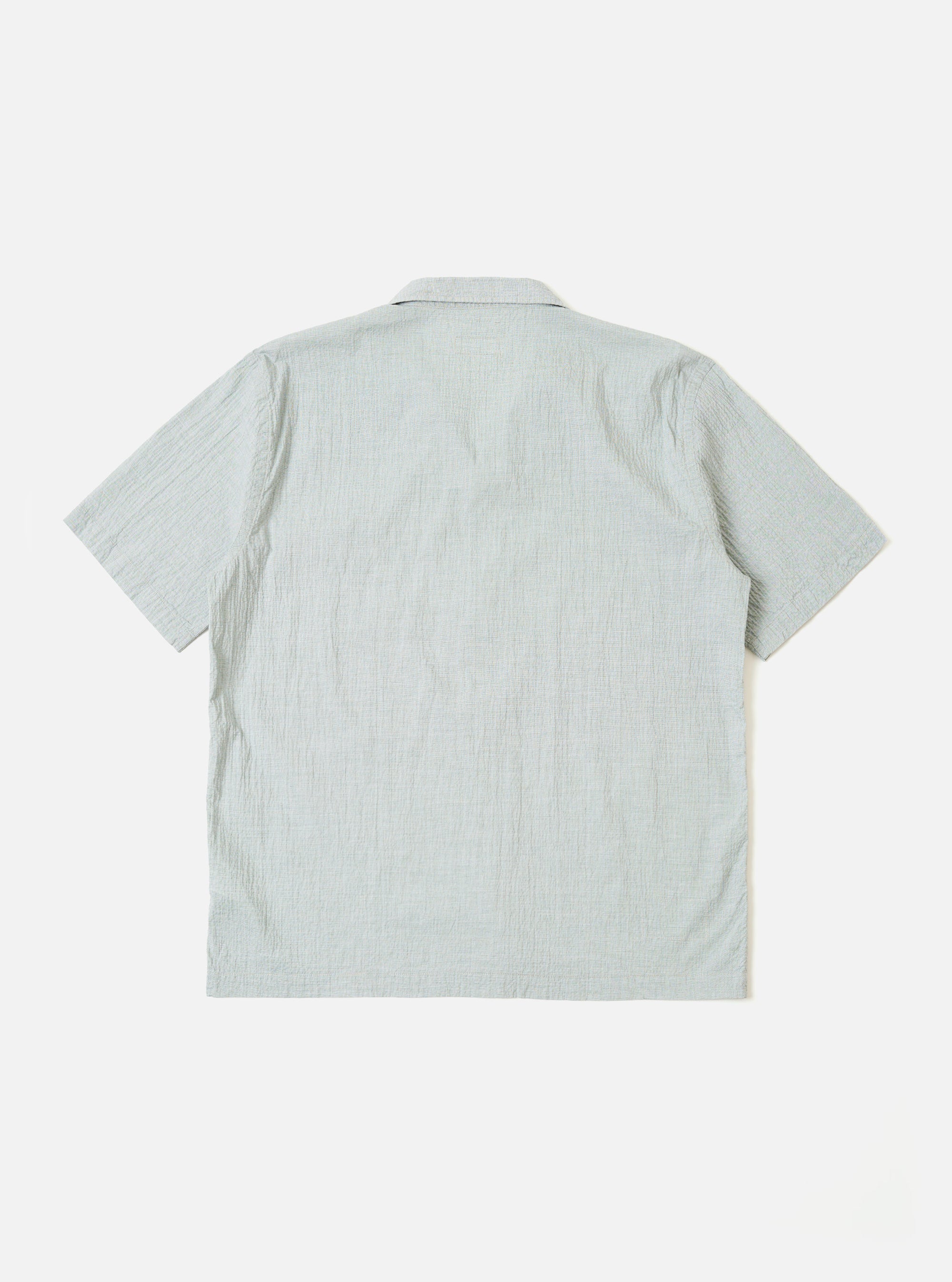The Green Seersucker Road Shirt is shown from a rear angle on a model. The shirt features a straight hem and short sleeves, with the textured seersucker fabric being prominent. The model is standing against a plain, light grey background. No mannequin is present in the image.