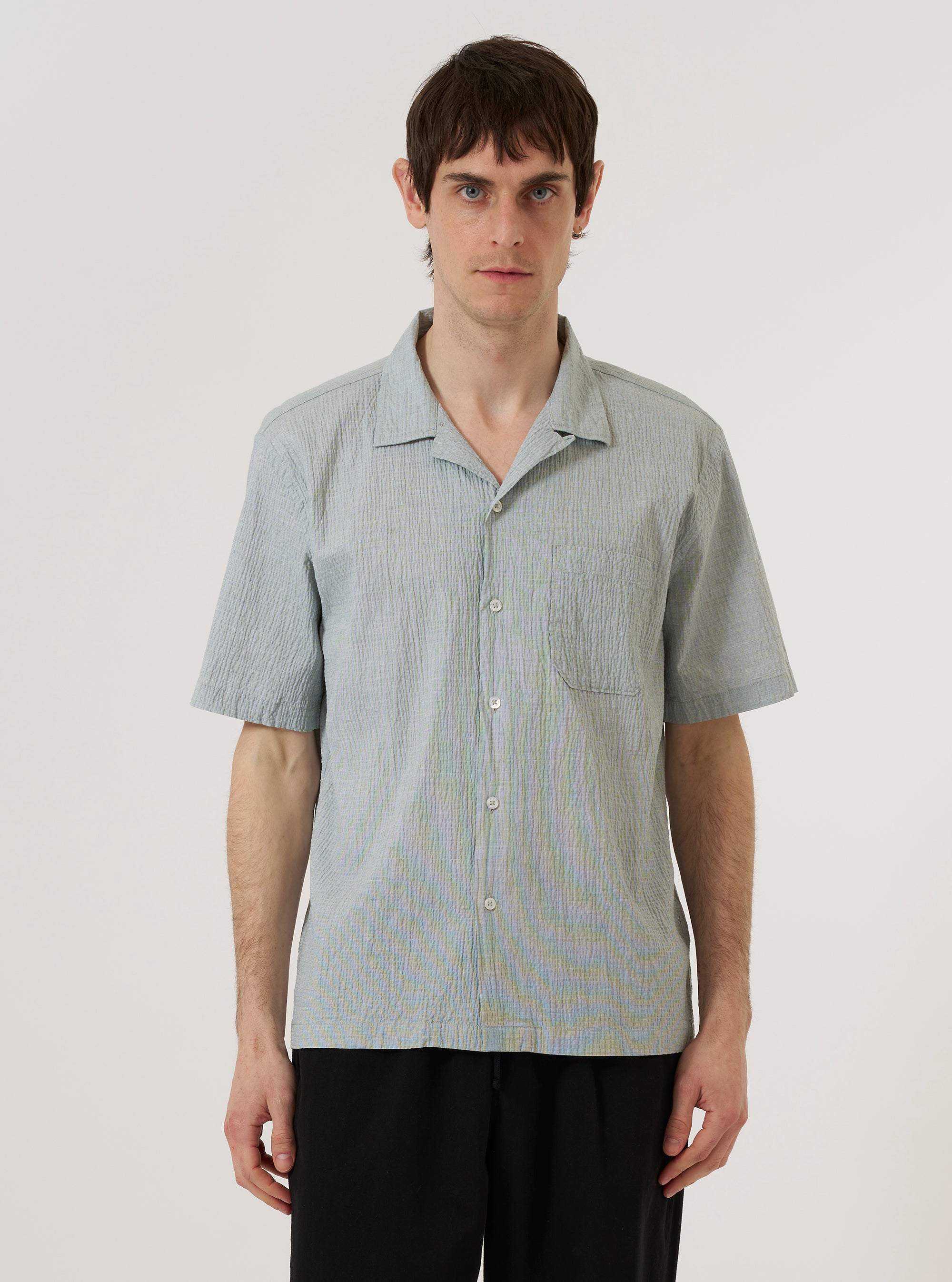 A model wears the Green Seersucker Road Shirt against a plain white background. The shirt features a camp collar, a five-button placket, and a single chest pocket. The fabric has a distinct puckered seersucker texture in a solid green color. The model is shown from the waist up.