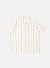 The Ecru/Navy/Sand Hendrix Stripe Road Shirt is shown as a flat lay against a plain white background. The shirt features a vertical stripe pattern in ecru, navy, and sand, a relaxed camp collar, and a central button-down front. It has short sleeves and a single patch pocket on the left chest.