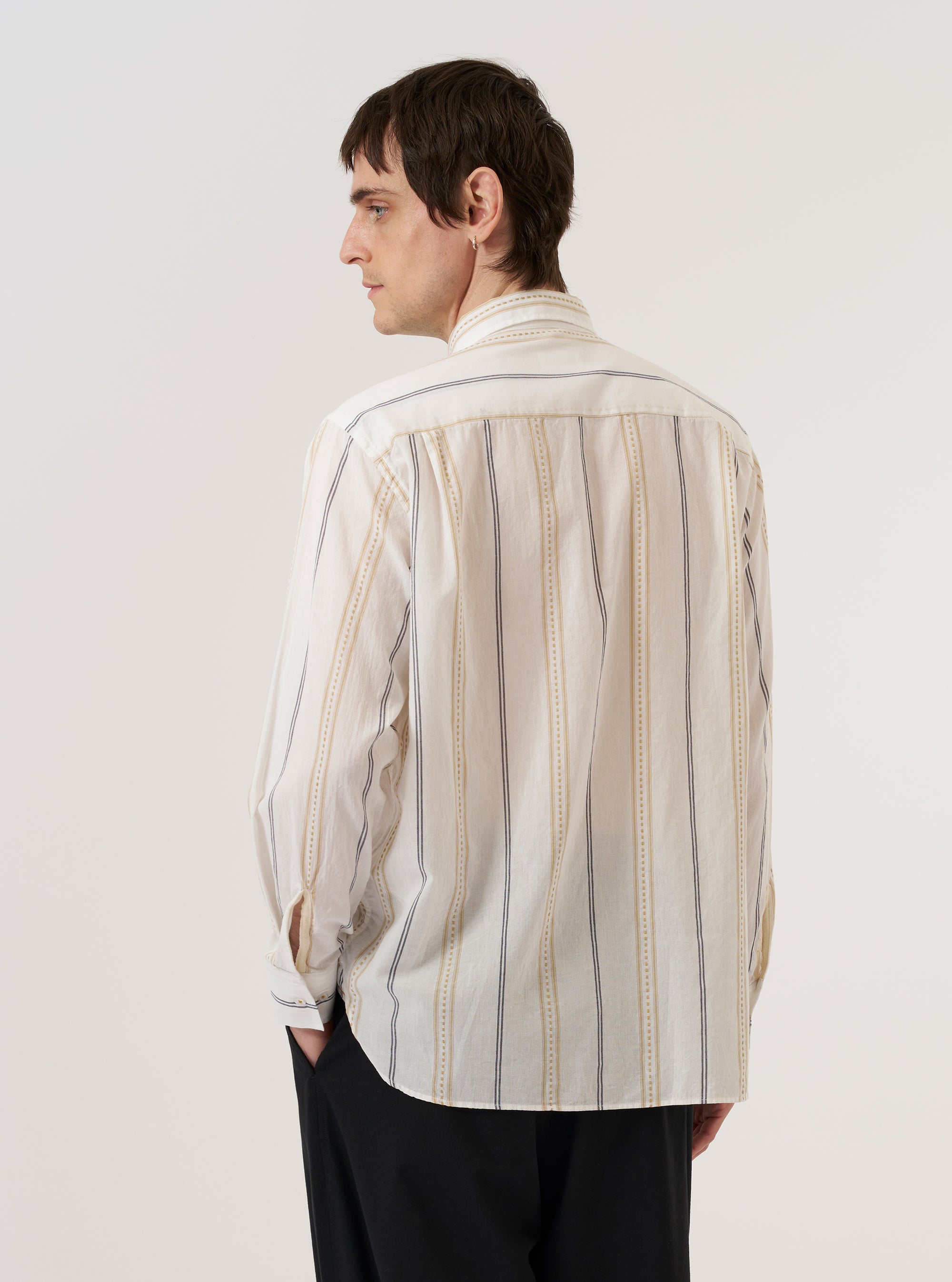 A model wears the Ecru/Navy/Sand Hendrix Stripe Square Pocket Shirt, shown from a rear three-quarter angle against a plain white background. The shirt features vertical stripes in ecru, navy, and sand, with a straight hem and short sleeves. The garment is constructed from a textured cotton fabric, and its relaxed fit and structured collar are prominent features.