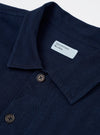 The Indigo Recycled Herringbone Attendant Shirt is displayed as a flat lay against a plain white background. The shirt features a distinct herringbone weave in a deep indigo blue with three prominent patch pockets on the front. It has a classic pointed collar, a full button-up front, and long sleeves with buttoned cuffs.