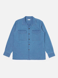 The Washed Indigo Recycled Herringbone Attendant Shirt is shown as a flat lay against a plain white background. The shirt features a flat collar, a full-length button-down front, and two large chest pockets with button-closure flaps. The washed indigo blue fabric displays a subtle herringbone texture and a straight hem with short side splits.