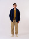 The Indigo Recycled Herringbone Kyoto Work Jacket is shown as a flat lay against a white background. The jacket features a wrap-front design with fabric ties, a chest patch pocket, and two large patch pockets at the waist. The indigo-dyed cotton fabric has a visible herringbone weave texture throughout.