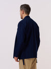 A model wears the Indigo Recycled Herringbone Kyoto Work Jacket, shown from the back against a plain white background. The jacket features a relaxed, kimono-style silhouette with a straight hem and mid-length sleeves. The indigo-dyed fabric displays a visible herringbone weave texture throughout the garment's rear panel. No mannequin is present in the image.