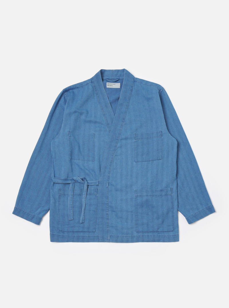 The Washed Indigo Recycled Herringbone Kyoto Work Jacket is shown as a flat lay against a white background. The jacket features a wrap-style front with fabric ties, two large patch pockets at the waist, and a single patch pocket on the left chest. The indigo-washed cotton fabric displays a distinct herringbone weave pattern.