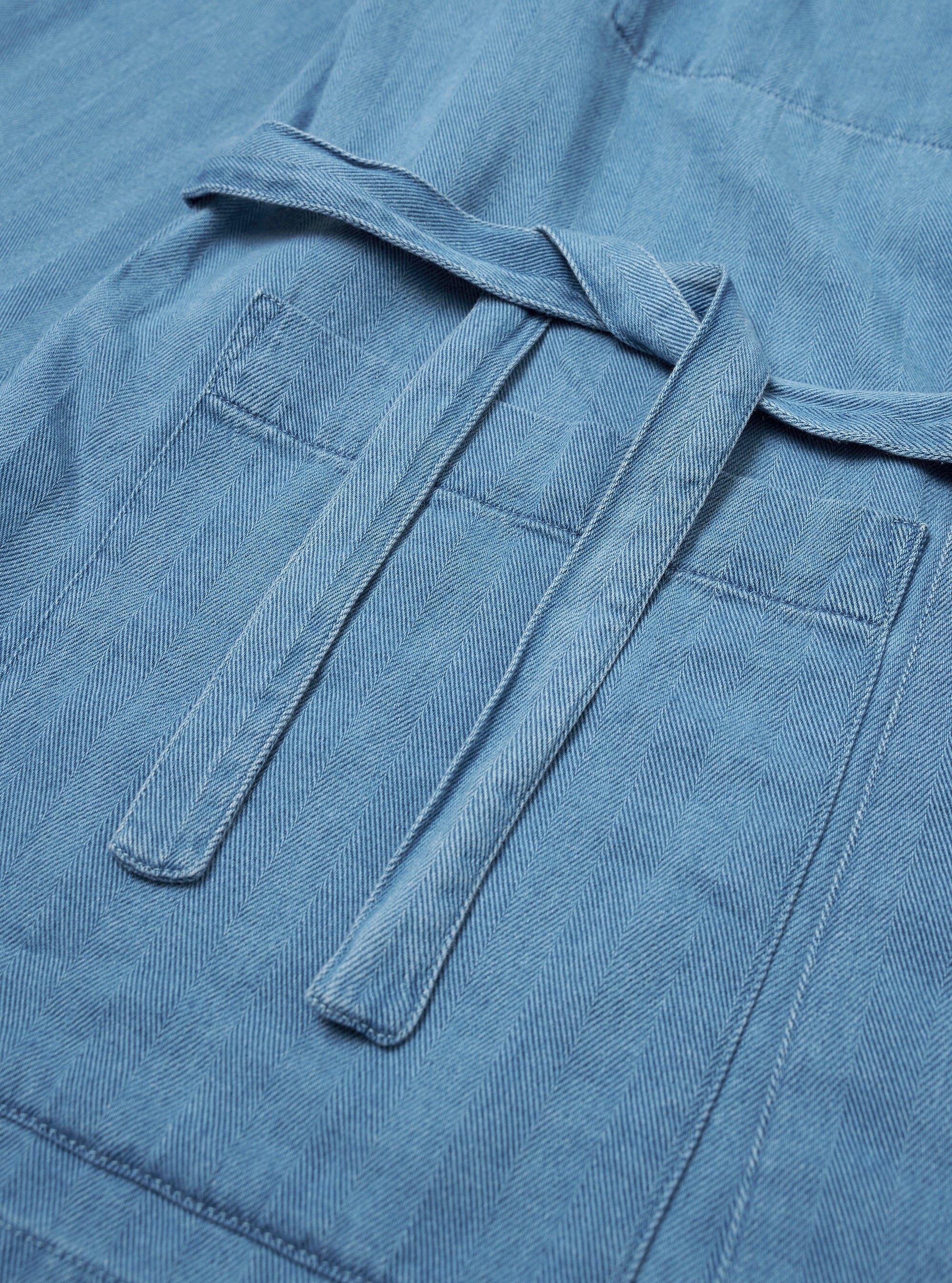 The Washed Indigo Recycled Herringbone Kyoto Work Jacket is shown from the back as a flat lay against a plain white background. The image highlights the jacket's straight hem, loose fit, and the distinct chevron pattern of the washed indigo herringbone fabric.