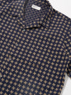 The Navy/Sand Rhodes 8 Cotton Road Shirt is shown from the back as a flat lay against a plain white background. The shirt features a clean, straight hem, short sleeves, and a single-piece collar. The fabric is a patterned 100% cotton in navy and sand.