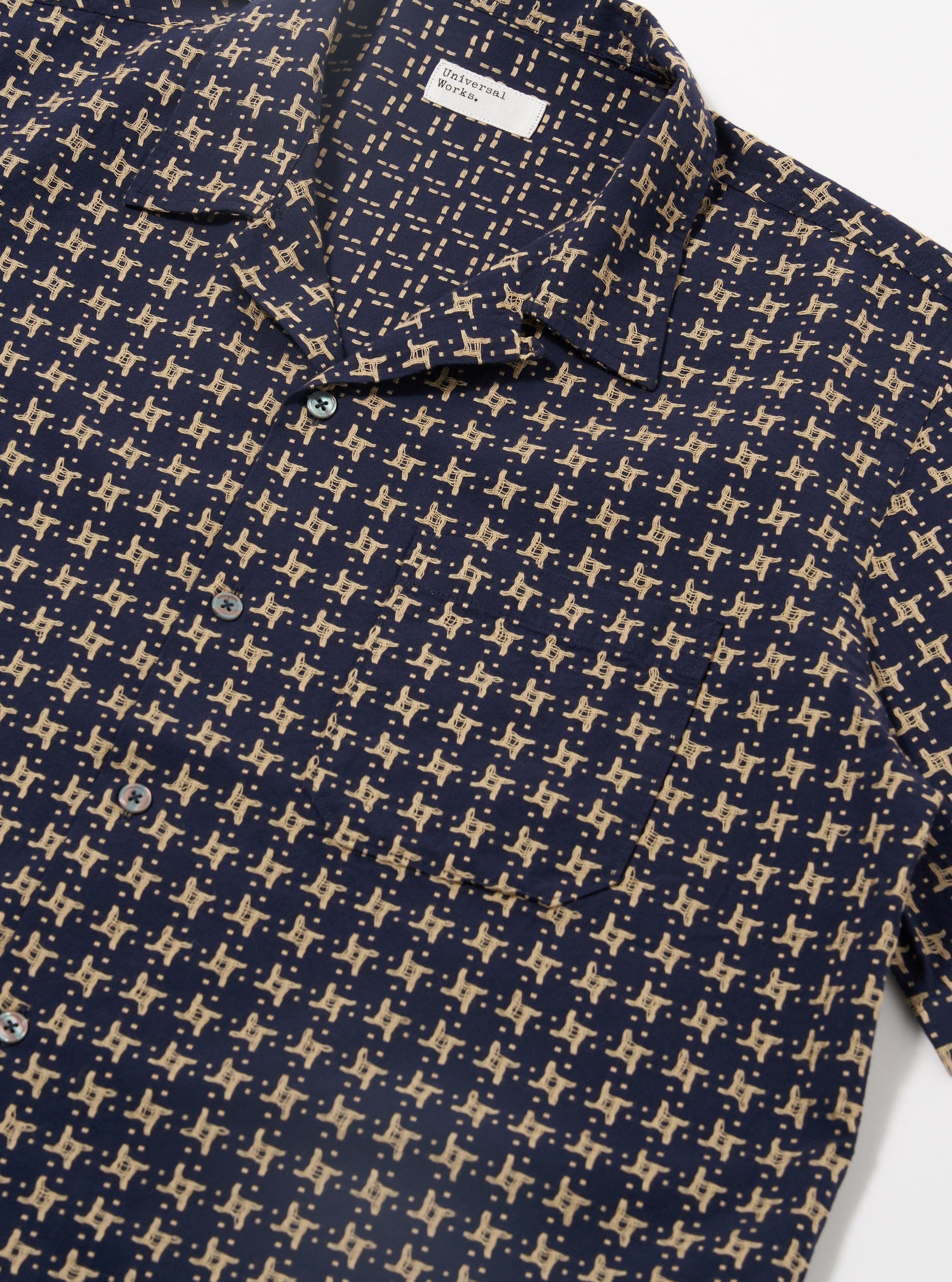 The Navy/Sand Rhodes 8 Cotton Road Shirt is shown from the back as a flat lay against a plain white background. The shirt features a clean, straight hem, short sleeves, and a single-piece collar. The fabric is a patterned 100% cotton in navy and sand.