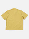 A model wears the Yellow Mykonos Cotton Road Shirt against a plain, neutral background. The short-sleeve shirt features a textured yellow and ochre pattern, a one-piece camp collar with a loop closure, and a single patch pocket on the left chest. The garment is shown with a regular fit and a straight hem.
