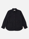 The Black Kendal Cotton Travail Overshirt is shown as a flat lay against a white background. The overshirt features a one-piece collar, a central button-down closure, and two large patch pockets at the waist. The black cotton fabric has a smooth texture, and the garment is finished with a curved hem.