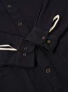 The Black Kendal Cotton Travail Overshirt is shown in a detail view as a flat lay against a plain white background. The image focuses on the texture of the black cotton fabric and the construction of a functional chest patch pocket.