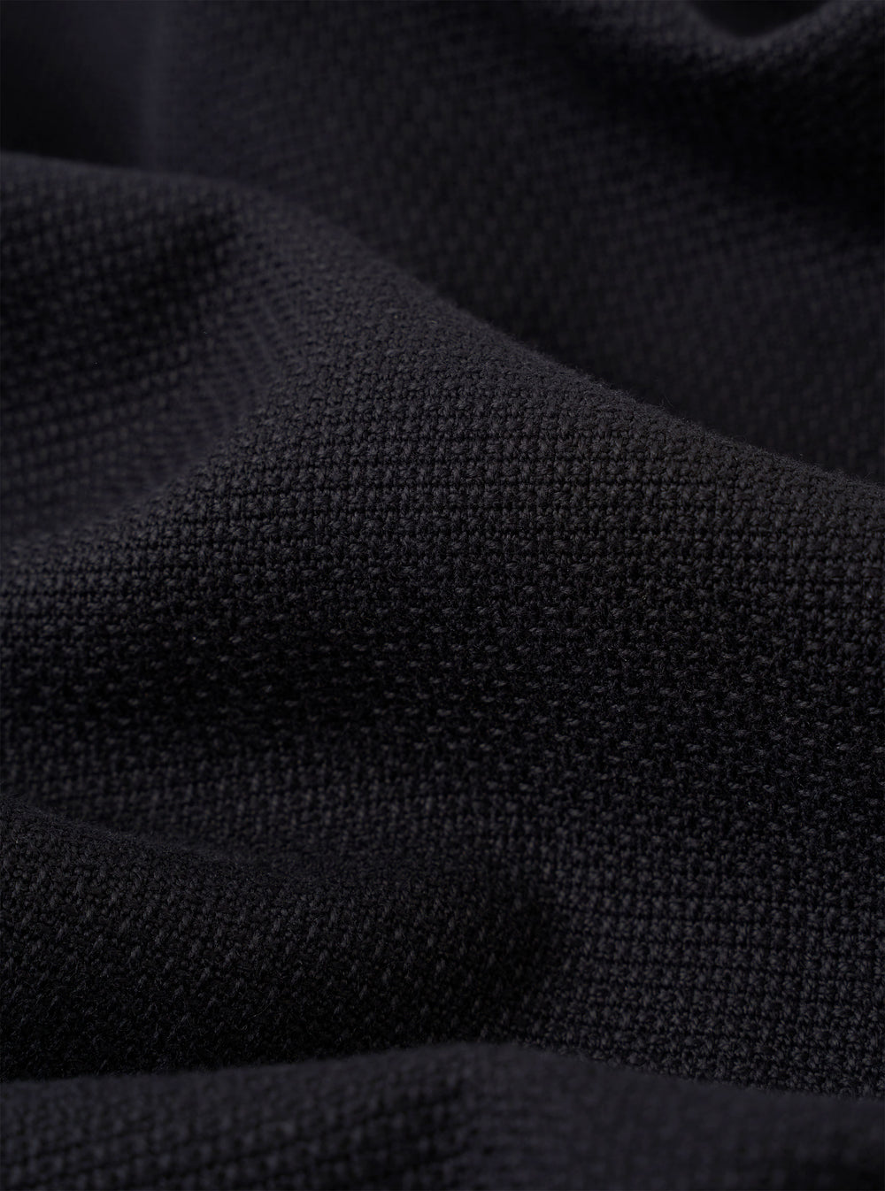 A close-up fabric swatch of the Black Kendal Cotton Travail Overshirt highlights the solid black color and the smooth, durable weave of the cotton fabric. The material fills the entire frame, providing a detailed view of the garment's texture.