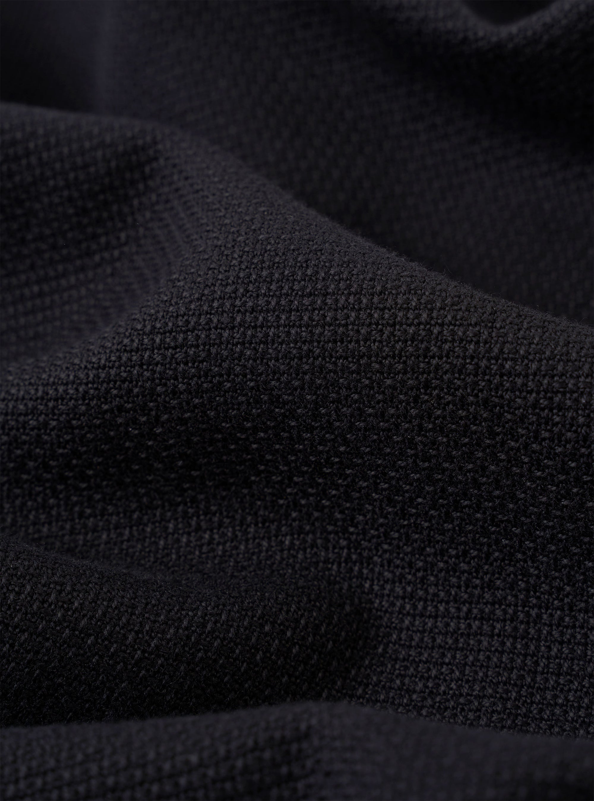 A close-up fabric swatch of the Black Kendal Cotton Travail Overshirt highlights the solid black color and the smooth, durable weave of the cotton fabric. The material fills the entire frame, providing a detailed view of the garment's texture.