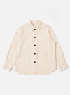 The Ecru Kendal Cotton Travail Overshirt is shown as a flat lay against a white background. The overshirt features a one-piece collar, a central button-down closure, and two large patch pockets at the waist. The garment is made from a textured ecru cotton fabric and has a curved hem with a visible contrast stitch insert.
