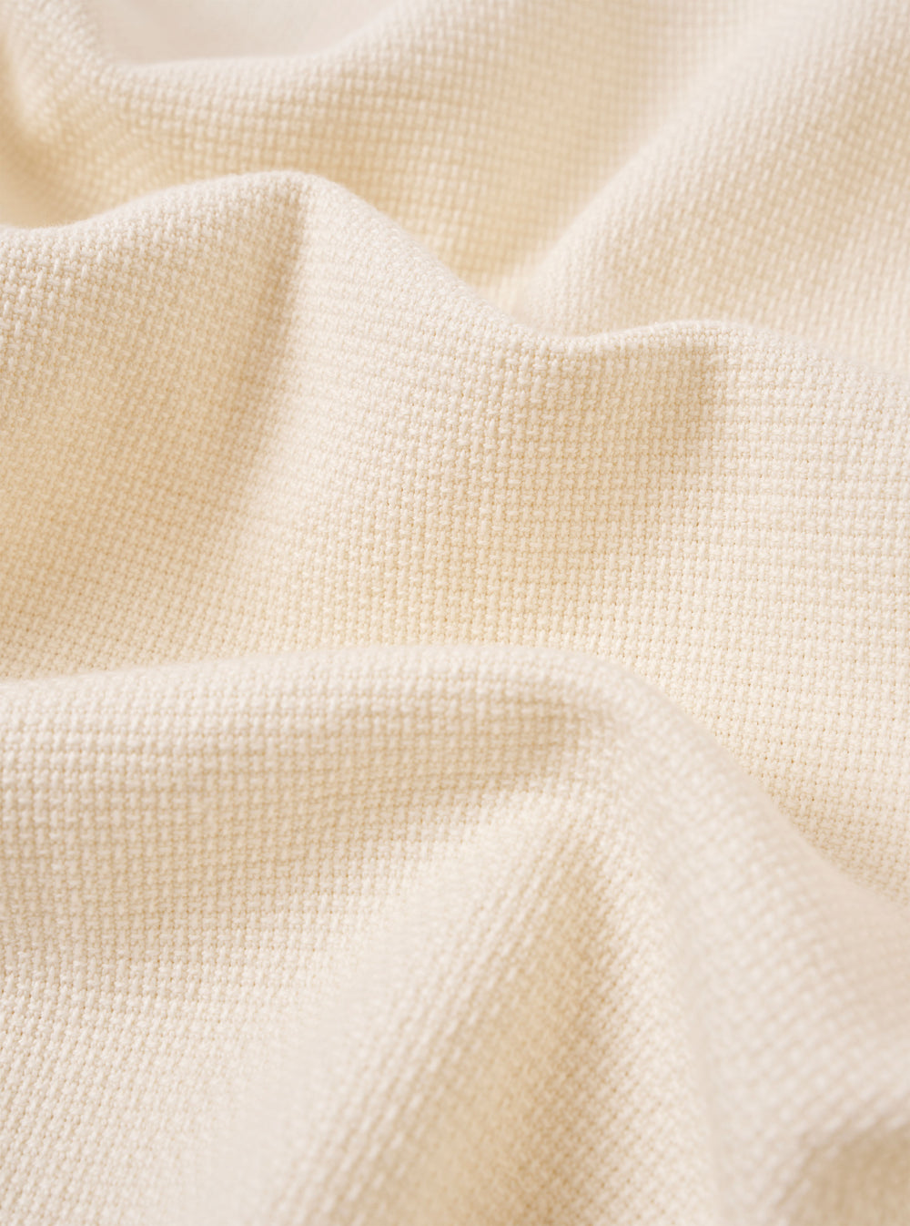 A close-up fabric swatch of the Ecru Kendal Cotton Travail Overshirt highlights the off-white, ecru color and the substantial, open-weave texture of the cotton fabric. The material fills the frame, providing a detailed view of the garment's weave and construction.