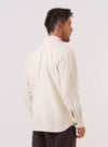 A model wears the Ecru Kendal Cotton Travail Overshirt, shown from the back against a plain white background. The image highlights the overshirt's loose, unstructured fit, a simple one-piece collar, and a curved hem. The fabric is a solid ecru cotton.