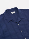 A model wears the Blue Maui Cotton Road Shirt over a white t-shirt against a plain white background. The short-sleeved shirt features a vertical blue and white stripe pattern, a camp collar, and a single chest pocket. The model is shown from the chest up, with the shirt left unbuttoned.