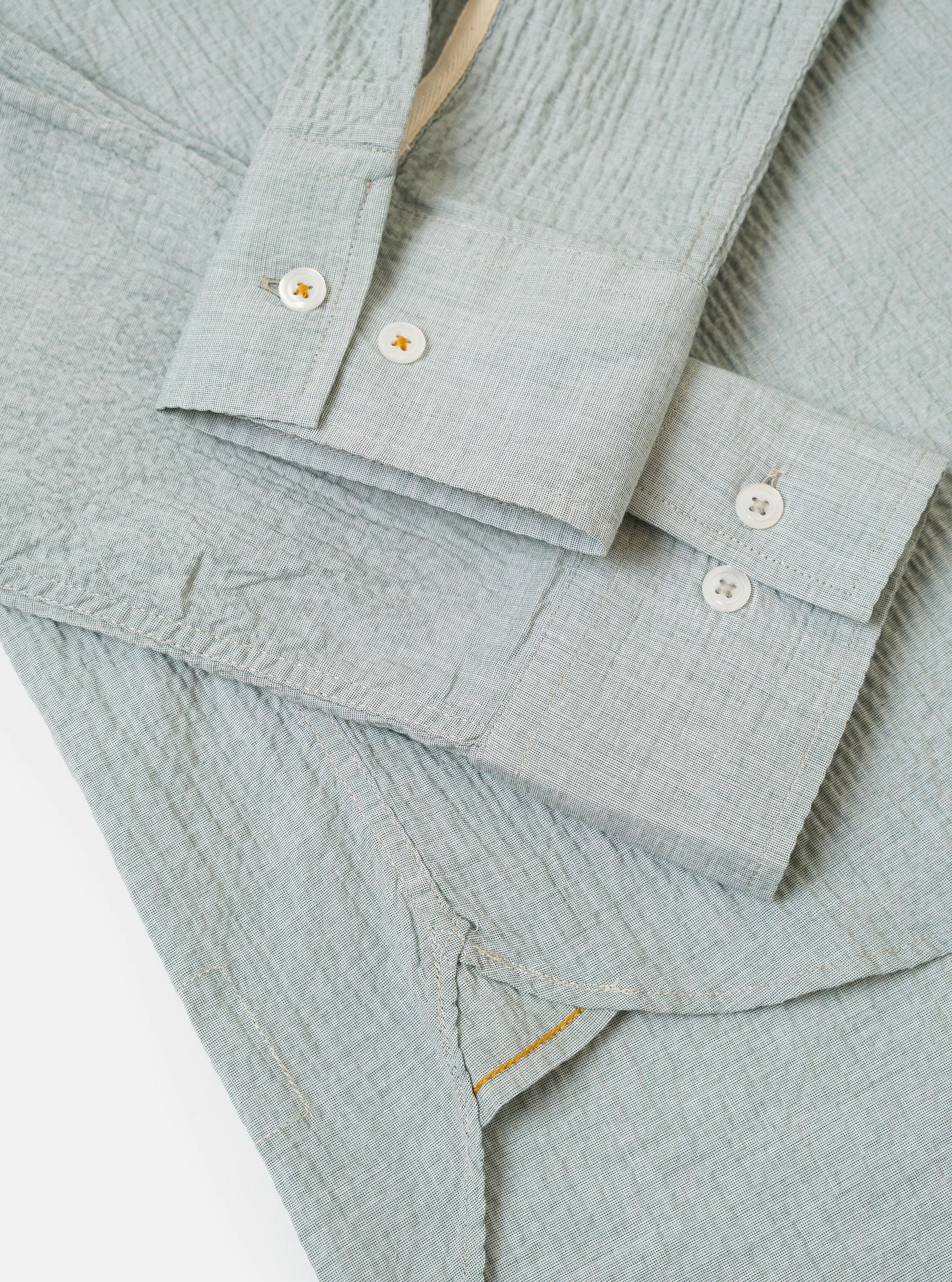 The Green Seersucker Square Pocket Shirt is shown from the back as a flat lay against a plain white background. The image highlights the straight hem, a simple back yoke, and the distinct puckered texture of the green seersucker fabric.
