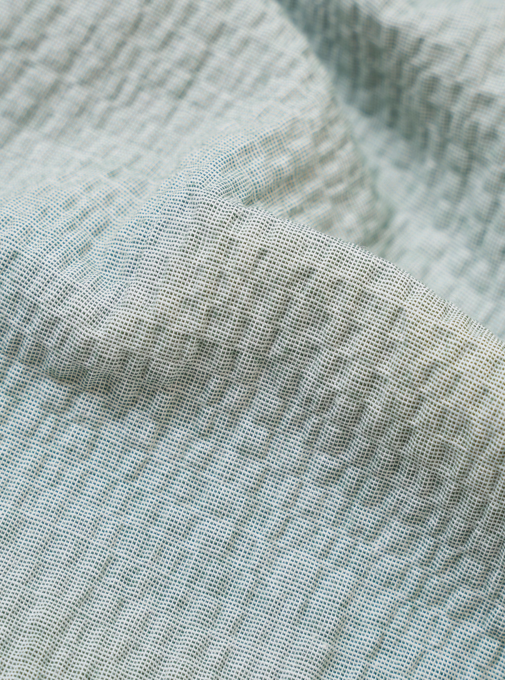 A close-up swatch image of the Green Seersucker Square Pocket Shirt fabric highlights the light green color and the distinct puckered texture of the seersucker material. The fabric fills the frame, providing a detailed view of the garment's weave and color.