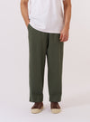 A model wears the Olive Kelly Cotton Judo Pant against a plain, neutral background. The trousers feature a relaxed, loose fit and are shown from the waist down, highlighting the comfortable drawstring waistband and the textured olive green cotton fabric. The straight-leg cut and functional design of the judo-style pants are the prominent features.