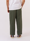 A model wears the Olive Kelly Cotton Judo Pant, shown from the waist down from a rear angle against a plain white background. The trousers are a solid olive green with a loose, relaxed fit and feature a comfortable waistband with a visible drawstring. The image highlights the clean construction and the straight, wide-leg silhouette of the cotton garment.