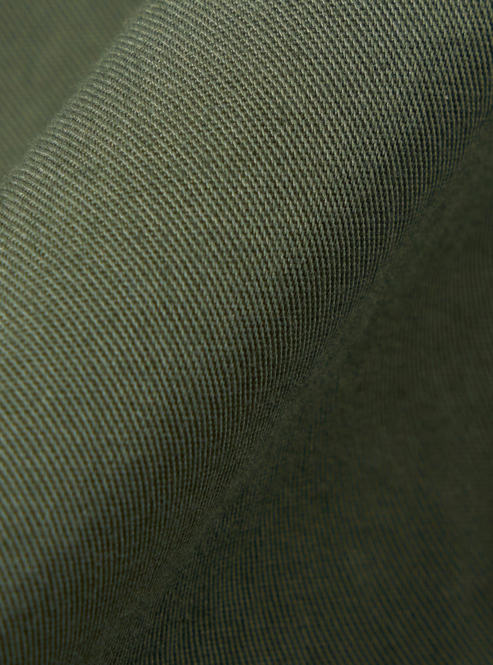 A close-up swatch of the Olive Kelly Cotton Judo Pant highlights the olive green color and the textured weave of the cotton fabric. The material fills the frame, providing a detailed view of the garment's color and construction.