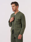 A model wears the Olive Kelly Cotton Glider Jacket against a plain white background. The jacket features a full-length front zipper, a pointed collar, and two large patch pockets located at the waist. The olive green cotton fabric appears structured and has a matte finish.