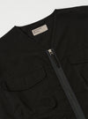 The Black Kelly Cotton Glider Jacket is shown from the back as it is worn by a model against a plain white background. The image highlights the clean, straight lines of the jacket's back panel and the bound edge detailing at the collar and hem. The model is also wearing olive green trousers.