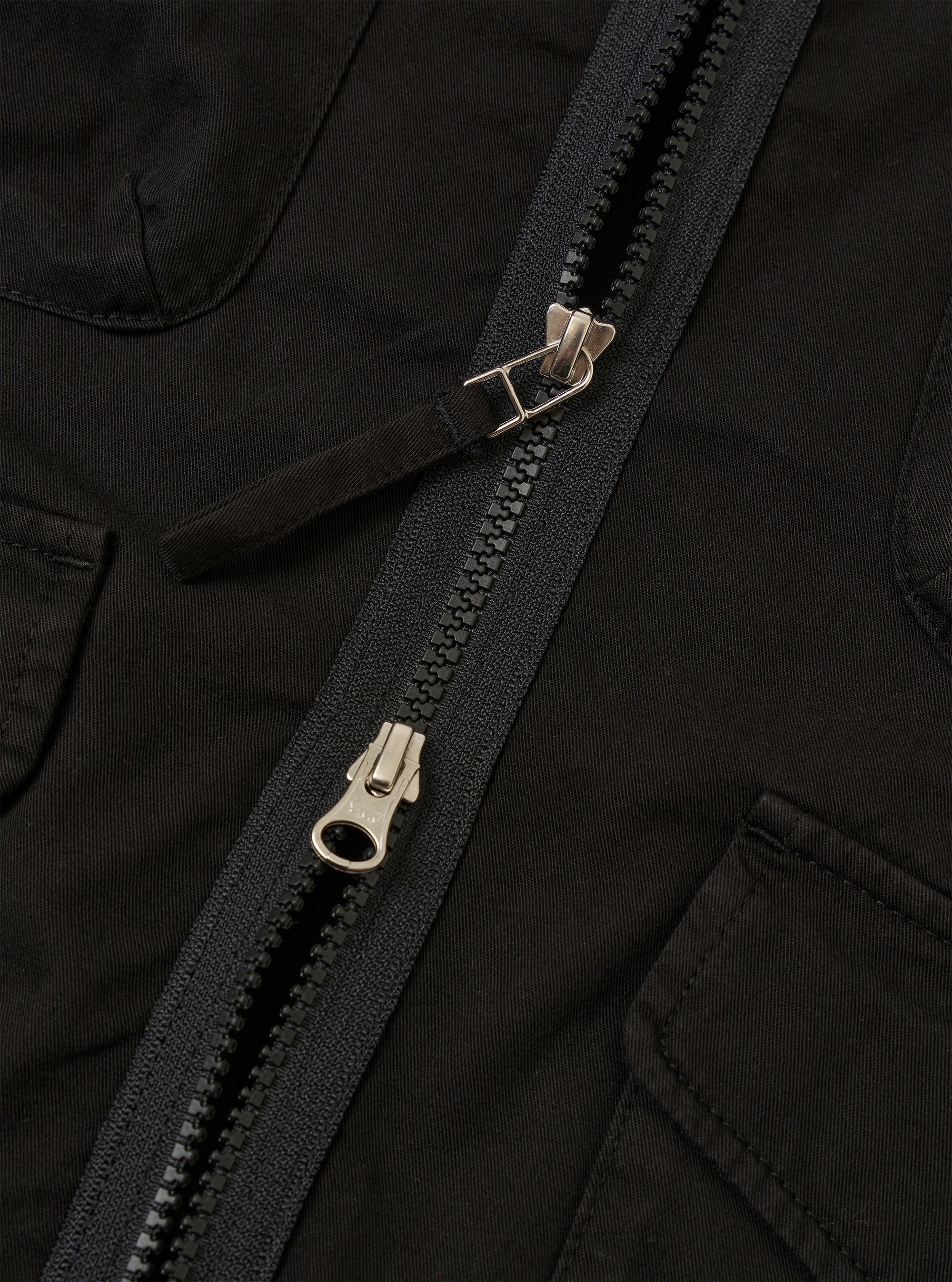 The Black Kelly Cotton Glider Jacket is shown as a flat lay against a white background. The jacket features two large flap chest pockets, a button-down front, and a classic pointed collar. The fabric has a smooth, solid black cotton finish with visible stitching details.