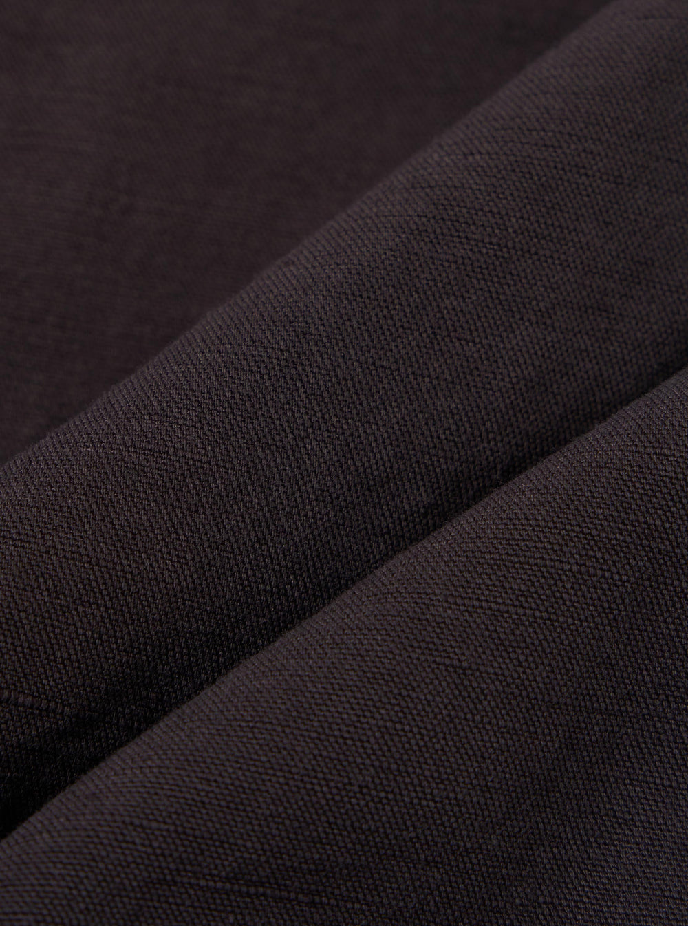A close-up fabric swatch of the Licorice Lyo Linen Mix Simple Short highlights the textured weave of the material. The image focuses on the dark brown fabric, showing the fine interlacing threads and natural variations in the linen mix. There is no model or mannequin present.