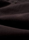 A close-up fabric swatch of the Licorice Lyo Linen Mix Oxford Pant highlights the deep brown licorice color and the subtle, natural texture of the linen and lyocell blend fabric. The image provides a detailed view of the garment's weave and material.