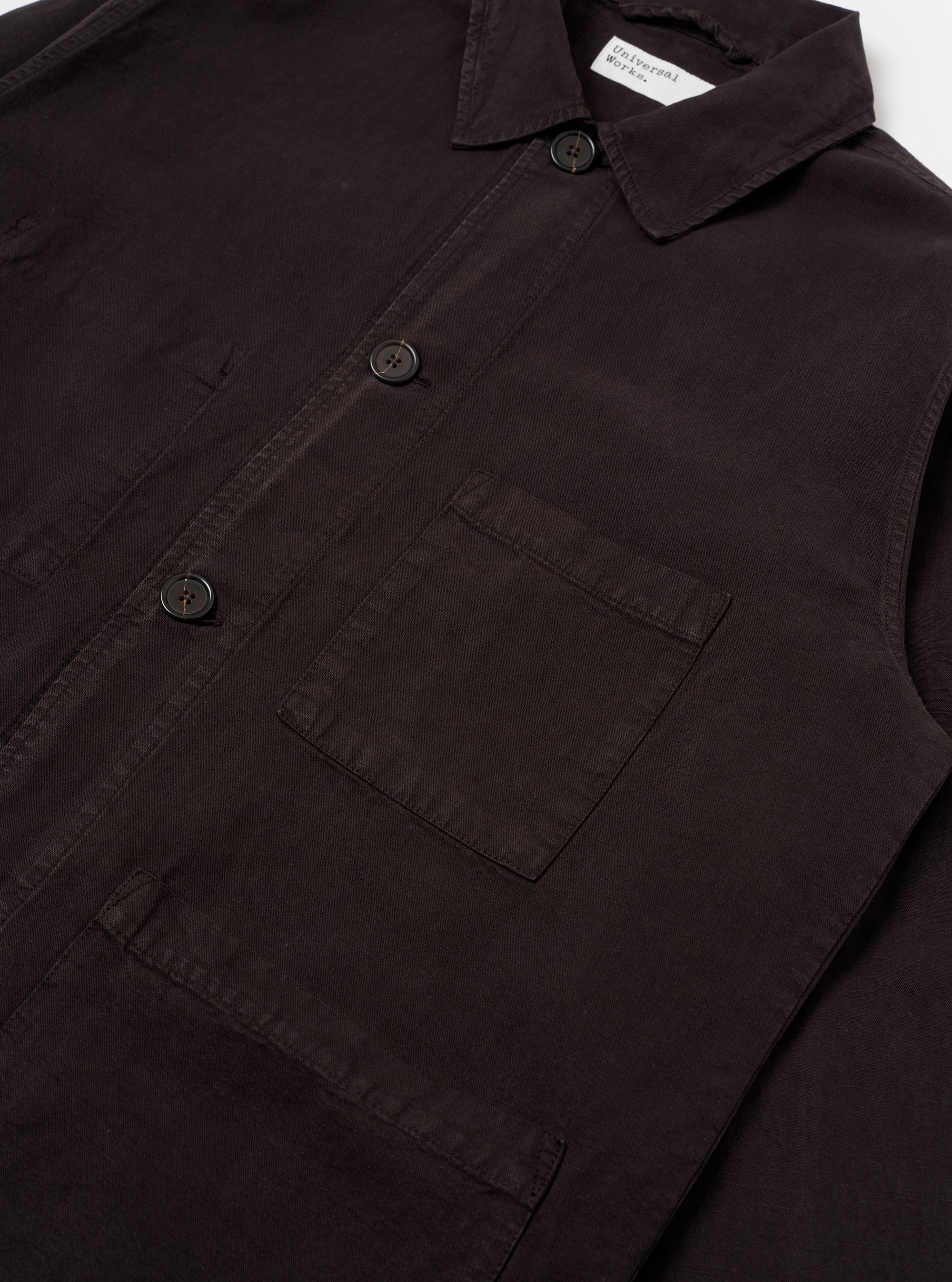 The Licorice Lyo Linen Mix Coverall Jacket is shown from a rear three-quarter angle as a flat lay against a plain white background. The image highlights the jacket's short, boxy silhouette, the straight hem, and the simple, unbuttoned cuffs. The dark brown fabric has a smooth, slightly washed appearance.