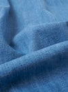 The Washed Indigo 8oz Slub Denim Field Jacket is shown in a detail view as a flat lay against a plain white background. The image highlights the textured slub denim fabric in a light indigo wash and the construction of a functional patch pocket with visible stitching.