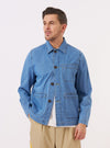 A model wears the Washed Indigo 8oz Slub Denim Field Jacket against a plain, neutral background. The jacket features a classic utility design with four large front patch pockets and a central button-down closure. The washed indigo denim has a visible slubby texture and a relaxed fit. The model is shown from the front, wearing the jacket over a light-colored top.