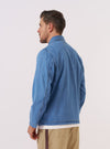 A model wears the Washed Indigo 8oz Slub Denim Field Jacket, shown from a rear three-quarter angle against a plain white background. The jacket is constructed from a textured washed indigo denim and features a straight hem and a simple back panel. The model is wearing the jacket over a light-colored top.