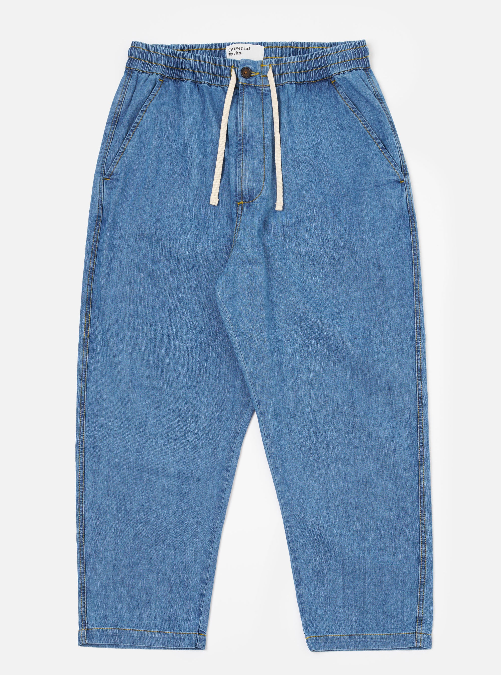 The Washed Indigo 8oz Slub Denim Hi Water Trouser is shown as a flat lay against a plain white background. The trousers feature an adjustable drawstring waist, two slanted front pockets, and a slightly cropped leg length. The 8oz slub denim fabric has a washed indigo finish with a visible textured appearance.