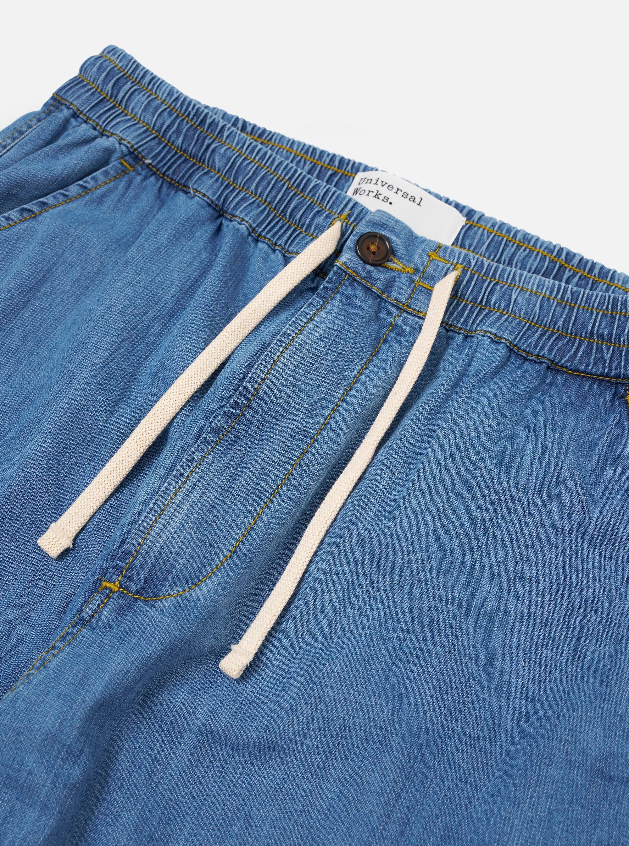 The Washed Indigo 8oz Slub Denim Hi Water Trouser is shown from the back as a flat lay against a plain white background. The image highlights the two rear patch pockets, the elasticated drawstring waistband, and the textured, washed indigo denim fabric.