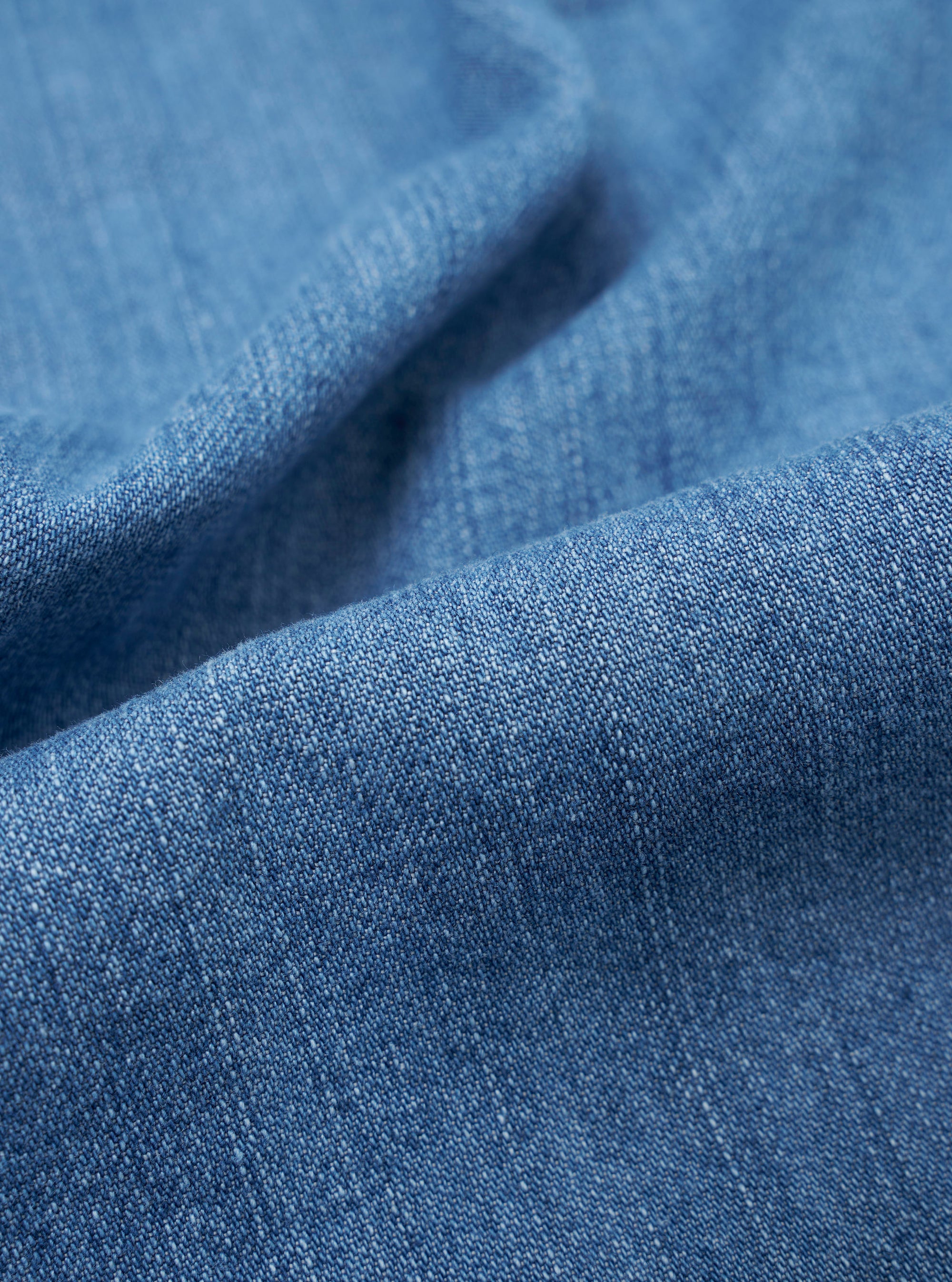 A close-up swatch image of the Washed Indigo 8oz Slub Denim Hi Water Trouser fabric highlights the textured, slubbed surface and the variations of the indigo blue wash. The weave of the 8oz denim is clearly visible, showing a mix of light and dark blue tones.