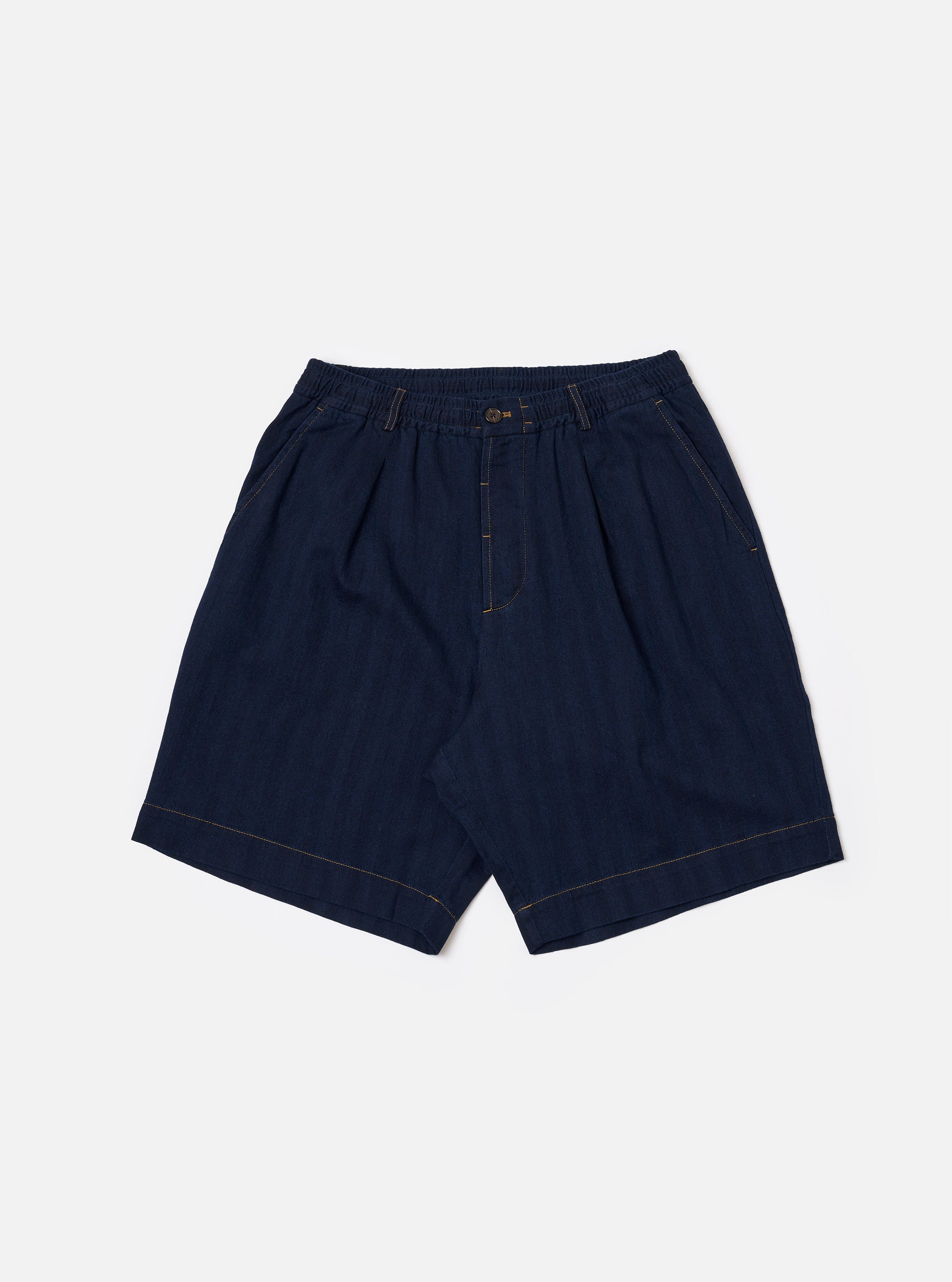 The Indigo Recycled Herringbone Pleated Track Short is shown as a flat lay against a white background. The shorts feature a visible herringbone weave pattern in indigo blue, front pleats, and an elasticated waistband with an adjustable drawstring.