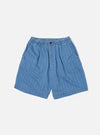 The Washed Indigo Recycled Herringbone Pleated Track Short is displayed as a flat lay against a white background. The shorts feature a relaxed fit with an elasticated waistband, an internal drawstring, a single front pleat on each leg, and two side pockets. The fabric is a washed indigo blue recycled cotton with a visible herringbone texture.