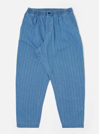 The Washed Indigo Recycled Herringbone Pleated Track Pant is shown as a flat lay against a white background. The trousers feature an elasticated waistband with an external drawstring, a single pleat at the front, and a loose, tapered leg. Two side pockets are visible, and the fabric displays a distinct herringbone texture in a washed indigo blue.