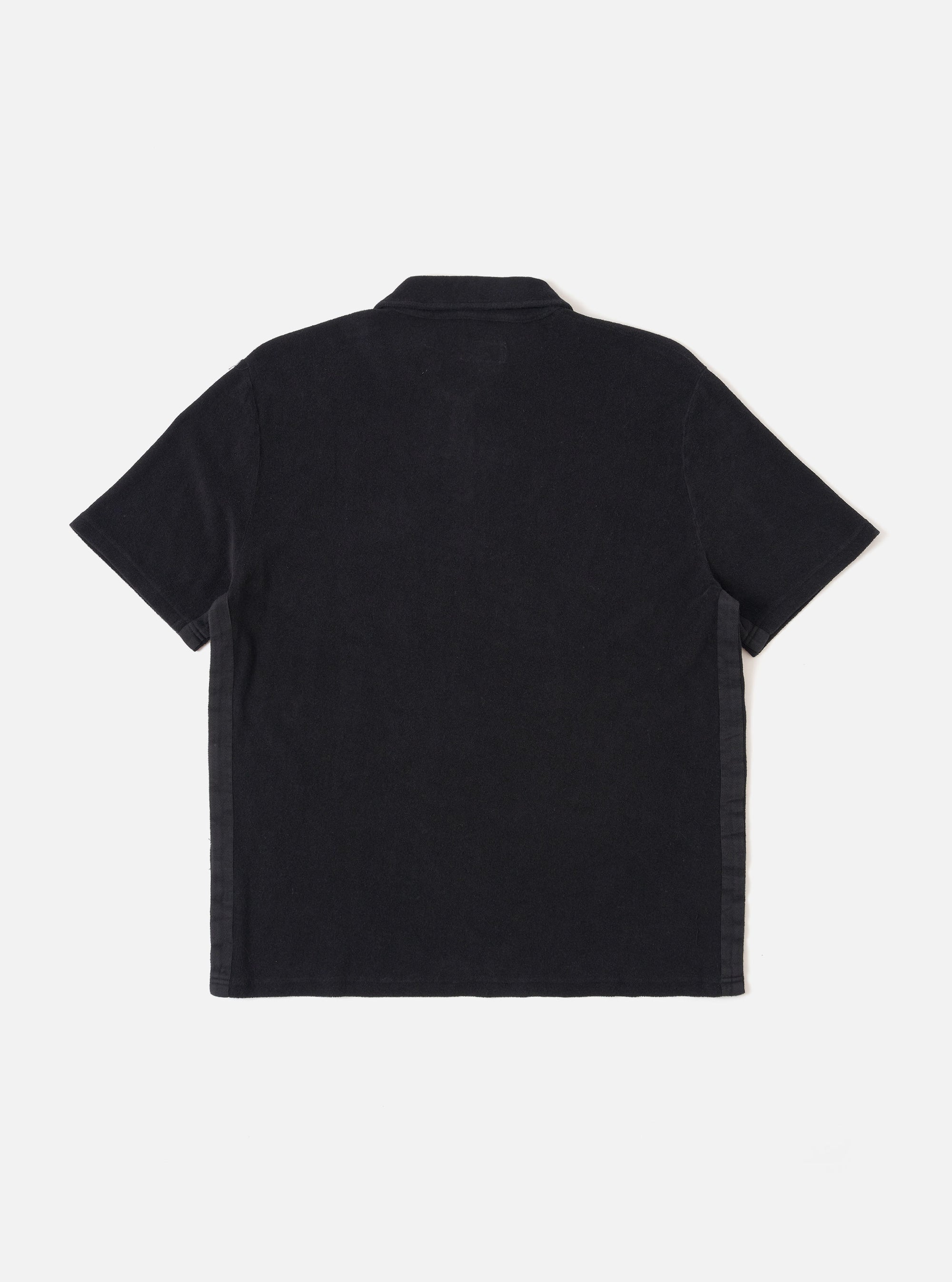 The Black Light Weight Terry Newlyn Polo is shown from the back as a flat lay against a plain white background. The image highlights the clean lines of the rear panel, the back of the collar, and the short sleeves. The black fabric features a visible, soft-textured light weight terry loop finish.