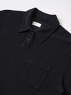 The Black Light Weight Terry Newlyn Polo is shown as a flat lay against a plain white background. The polo features a classic collar, a three-button placket, and a single patch pocket on the left chest. The black cotton fabric has a visible, soft terry texture with a fluffy, fleece-like appearance.