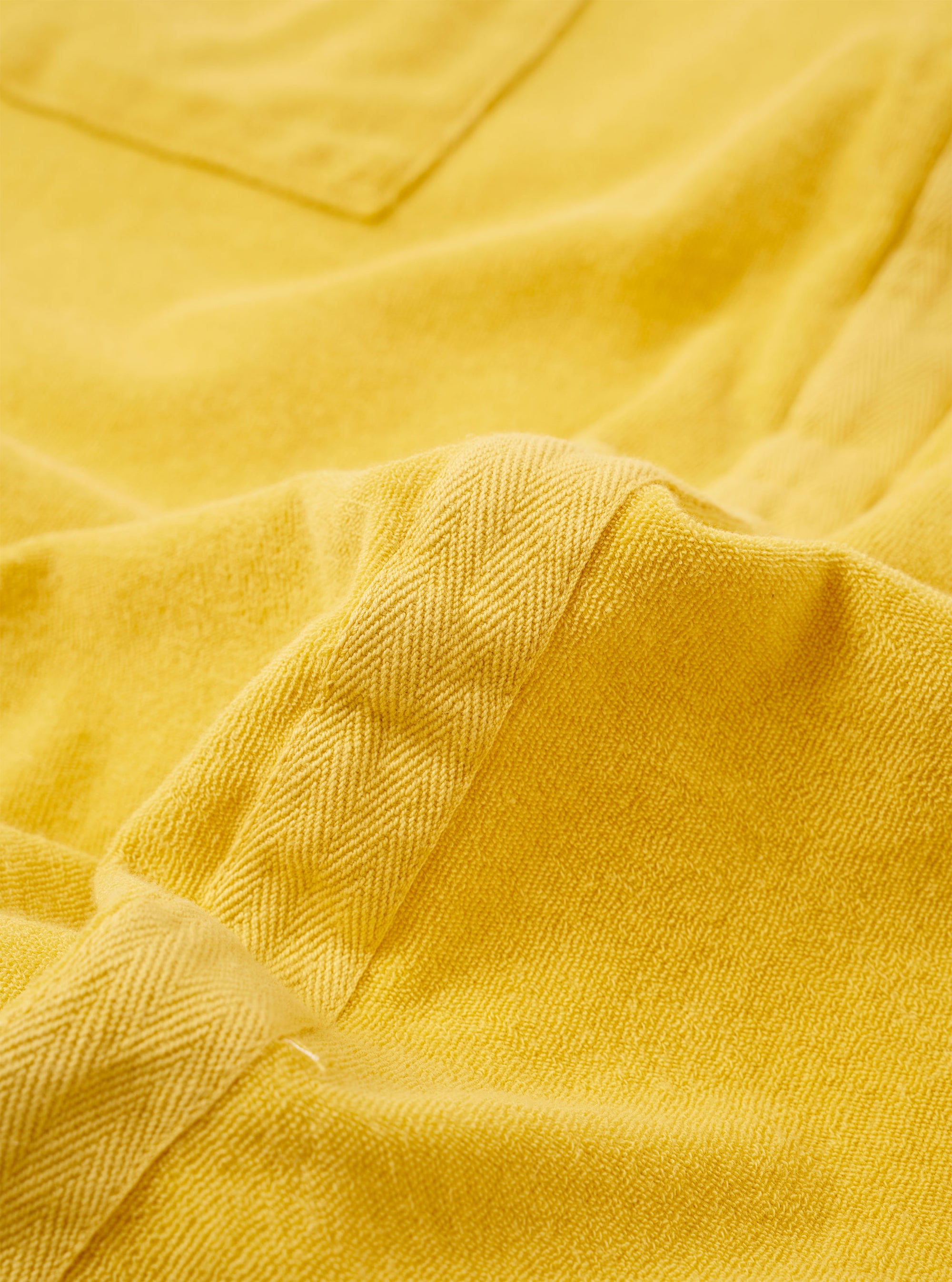 The Yellow Light Weight Terry Newlyn Polo is shown as a flat lay against a plain white background. The polo features a classic collar, a short sleeve design, and a single patch pocket on the left chest. The vibrant yellow fabric has a distinct, soft looped terry texture.