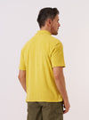 A model is wearing the Yellow Light Weight Terry Newlyn Polo, shown from the back against a plain white background. The polo features a relaxed fit, short sleeves, and a simple straight hem. The fabric is a vibrant yellow light-weight cotton terry with a soft, textured appearance. The model is shown from the waist up, highlighting the garment's clean construction.