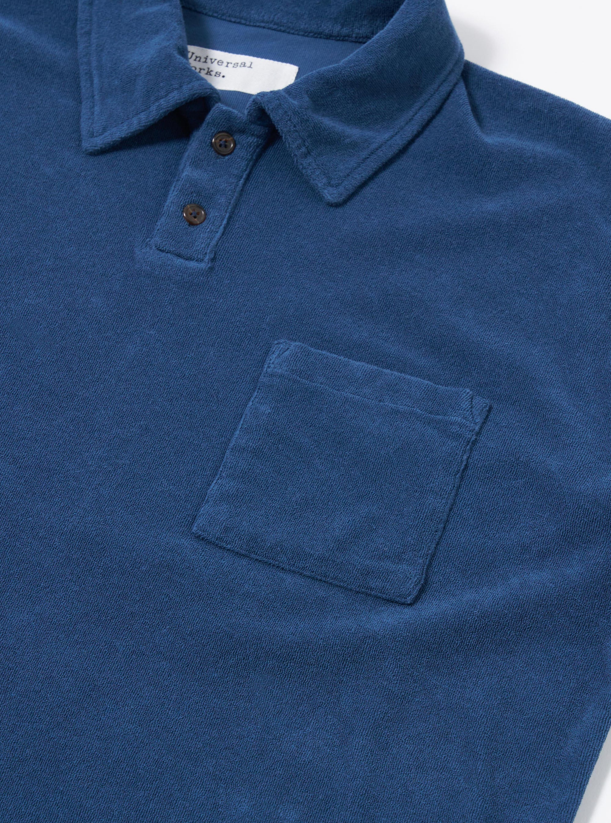 The Navy Light Weight Terry Newlyn Polo is displayed from the back as a flat lay against a plain white background. The image highlights the simple one-piece collar, the straight hem with side splits, and the soft texture of the navy blue light weight terry fabric.