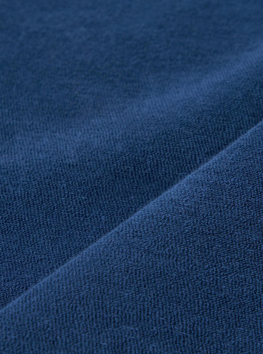 A close-up swatch image of the Navy Light Weight Terry Newlyn Polo fabric displays a deep navy blue color with a soft, looped terry cloth texture. The material is shown as a detailed textile sample against a neutral background.