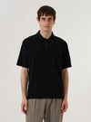 A model wears the Black Light Weight Terry Newlyn Polo against a plain white background. The polo shirt features a classic collar, a three-button placket, and short sleeves. The fabric is a solid black with a soft, textured light-weight terry finish. The model is shown from the waist up in a front-facing view.